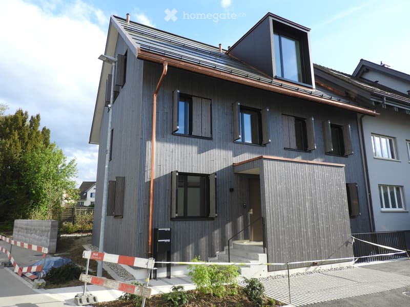 Modern two-story house with grey wooden facade, large windows, and a raised ground floor entrance.