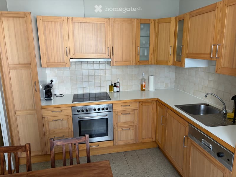 Modern kitchen with light wooden cabinets, stainless steel oven, sink, and coffee maker on the counter.