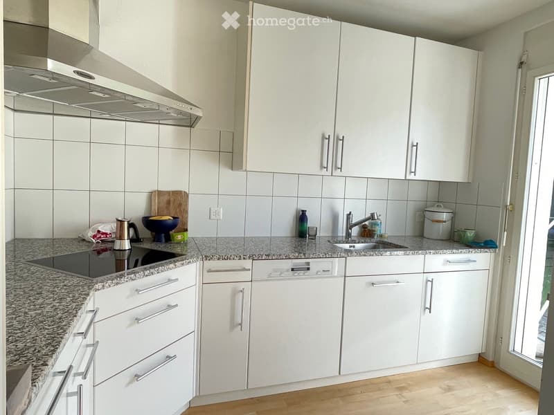 Modern kitchen with white cabinets, granite countertops, and stainless steel appliances including a dishwasher and electric stove. A sink with a modern faucet is visible, along with various kitchen items on the counter.