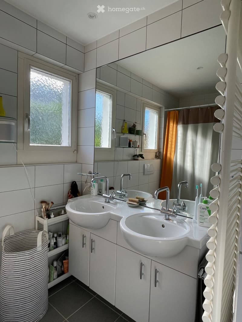 Modern bathroom with double sink vanity, mirrored cabinet, and tiled walls. Includes various toiletries and a towel rack.