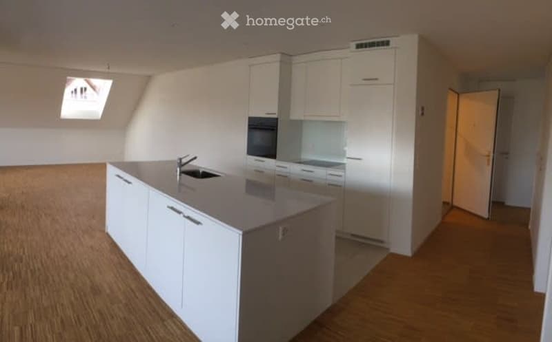 Modern kitchen with white cabinets, a central island, and a sink. The space is bright with wooden flooring and a skylight window.