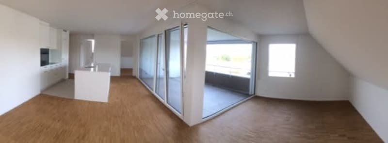 Bright, open-plan attic space with wooden flooring, large glass sliding doors leading to a balcony, and white cabinetry in the background.
