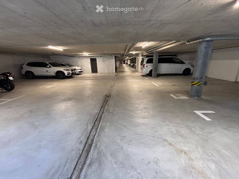 Underground parking area with several parked cars and a motorcycle, concrete floors and pillars, marked parking spaces.
