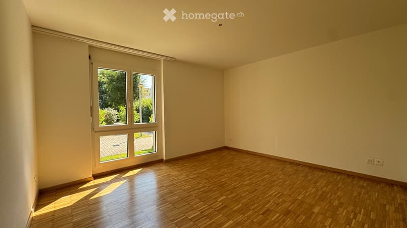 Empty room with wooden flooring and large windows, allowing natural light to fill the space. The walls are painted a light neutral color, and the room has a clean, minimalist design.
