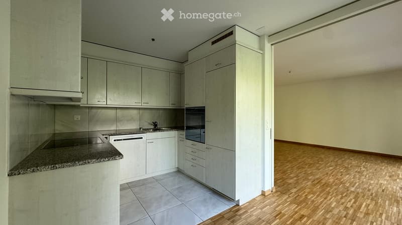 Modern kitchen with light-colored cabinets, granite countertop, stainless steel appliances, and a separate living area with wooden flooring.