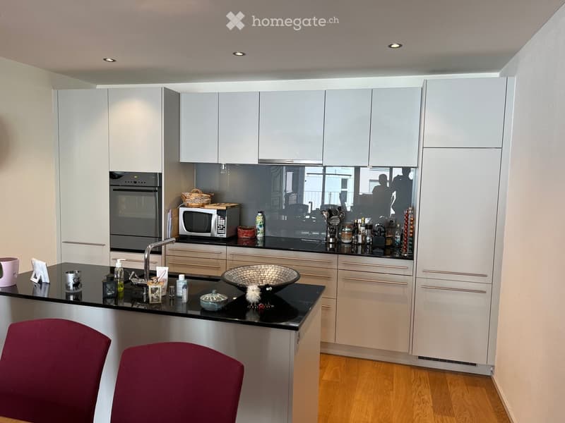 Modern kitchen with white cabinets, black countertops, and stainless steel appliances. Features a sink with a modern faucet, microwave, oven, and various kitchen items on the counter.