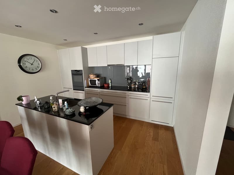 Modern kitchen with white cabinets, black countertops, and stainless steel appliances. Features a central island with a sink and various small decorative items.