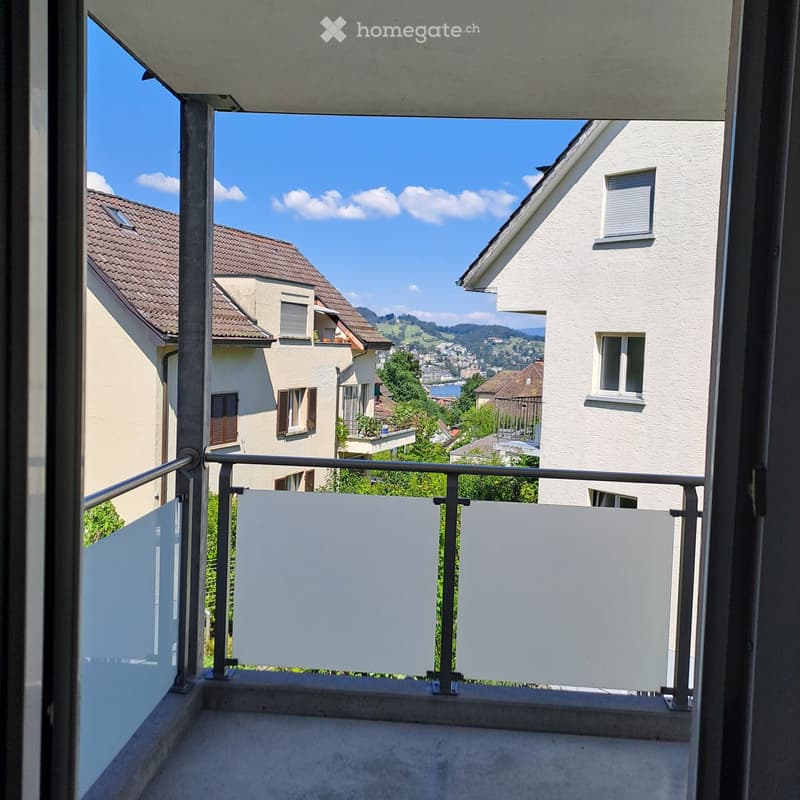 Balcony with metal railing and white privacy screens, overlooking a scenic town with houses, trees, and distant mountains.