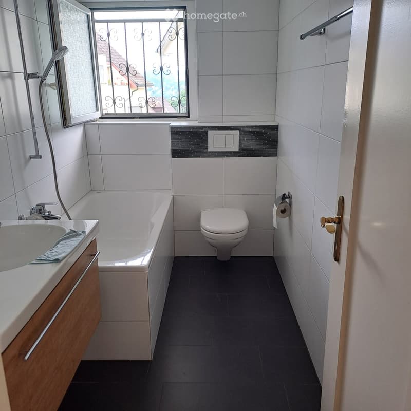 Modern bathroom with white tiles, bathtub, toilet, sink, and a window with decorative metal bars.