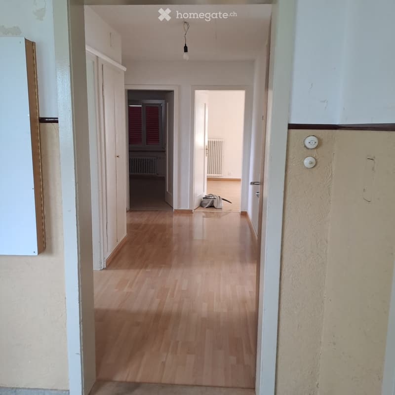 Empty hallway with wooden flooring, white walls, and several doors leading to other rooms.