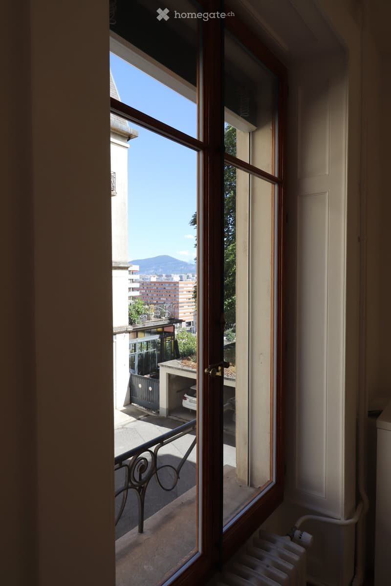 Balcony with metal railing, overlooking a parking area and cityscape with buildings and mountains in the background.