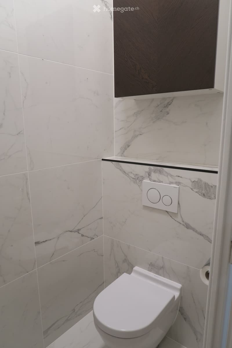 Modern bathroom with marble tiles, a white toilet, a control panel, and a toilet paper holder.
