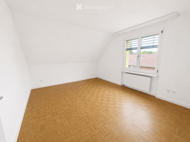 Empty room with wooden herringbone flooring, white walls, and a large window with blinds. The room has a radiator below the window and electrical outlets on the walls.