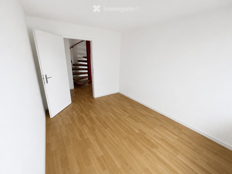 Empty room with light wooden flooring and white walls, featuring an open doorway leading to a staircase.