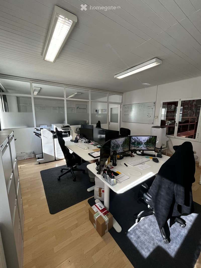 modern office with white desks, black chairs, multiple monitors, printers, whiteboard, wooden floor, cabinets, boxes