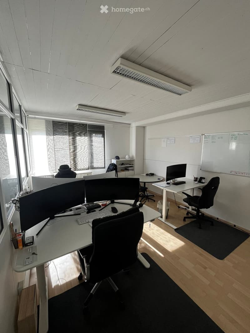 An office space with multiple desks, chairs, monitors, keyboards, and whiteboards.