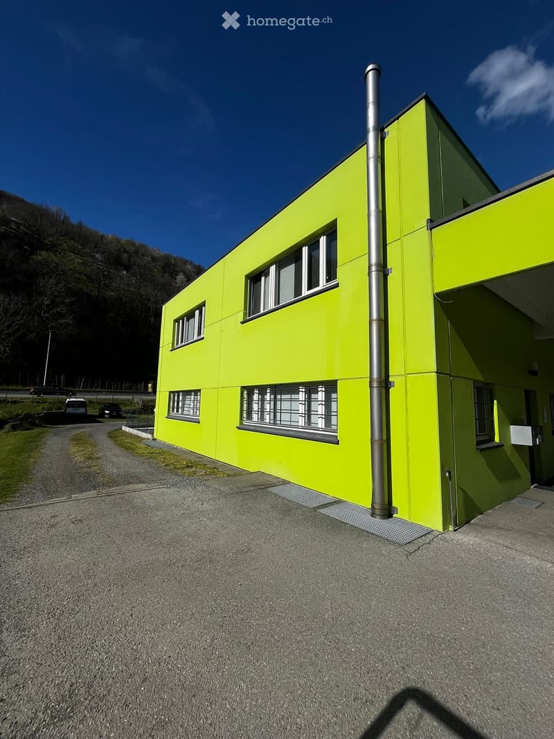 2 story building, yellow exterior, multiple windows, metal pipe, paved road, grassy area