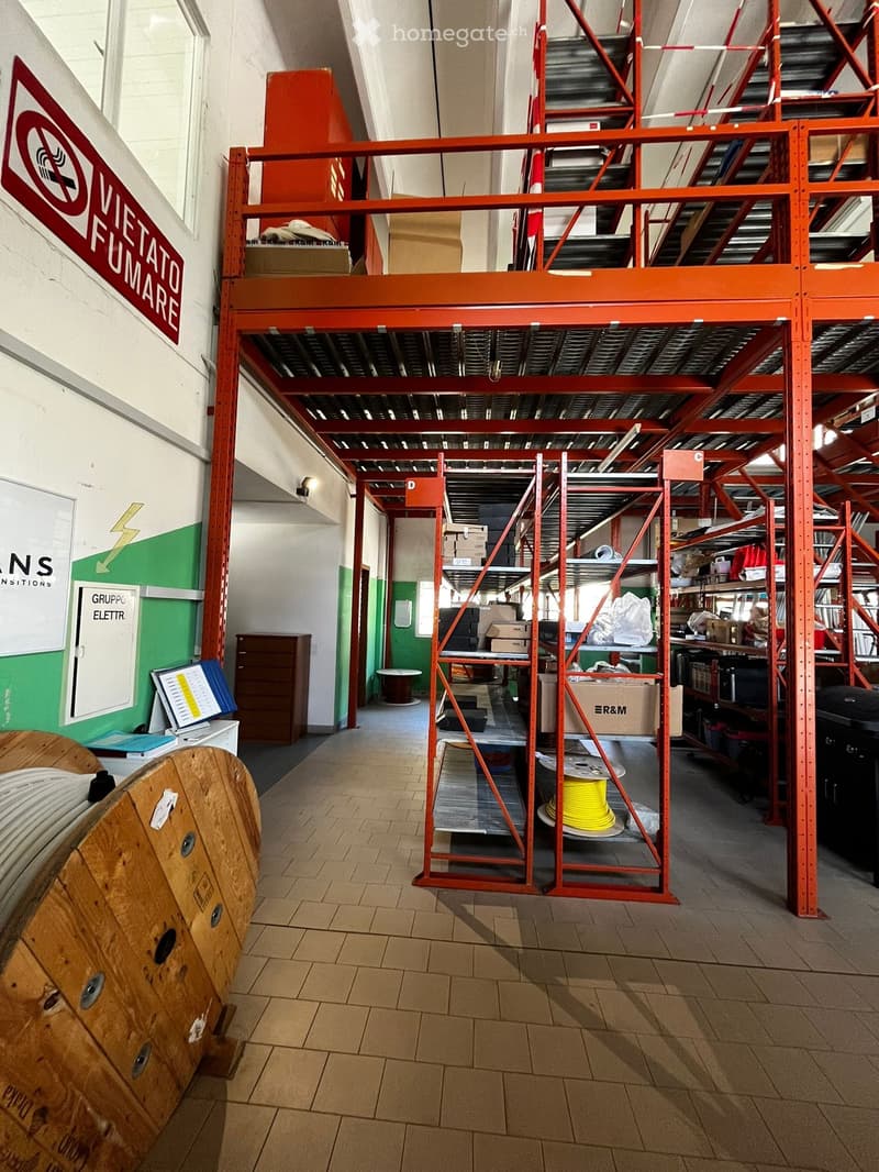 Warehouse with red metal shelving, storage boxes, wooden spools, and a sign indicating 'No Smoking'.