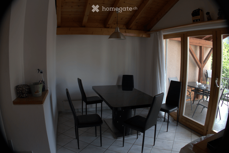 Dining area with a black table and four chairs, a hanging lamp, and a view to a wooden terrace through large glass doors.