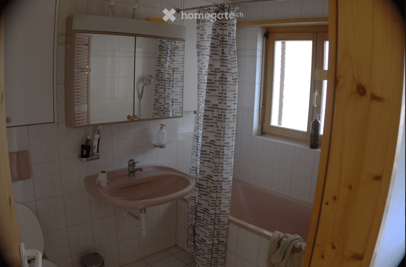 Bathroom with a pink sink, mirror cabinet, bathtub with a shower curtain, and a window with wooden frame. Includes a toilet, a cup on the sink, and a bottle on the windowsill.