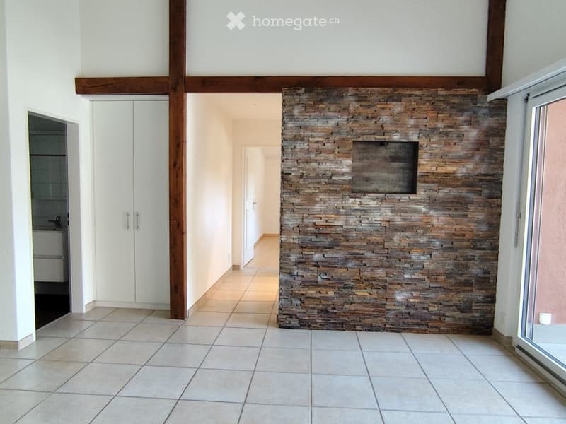 Empty room with white tiles, white walls, wooden beam, stone wall, glass door, white cabinets