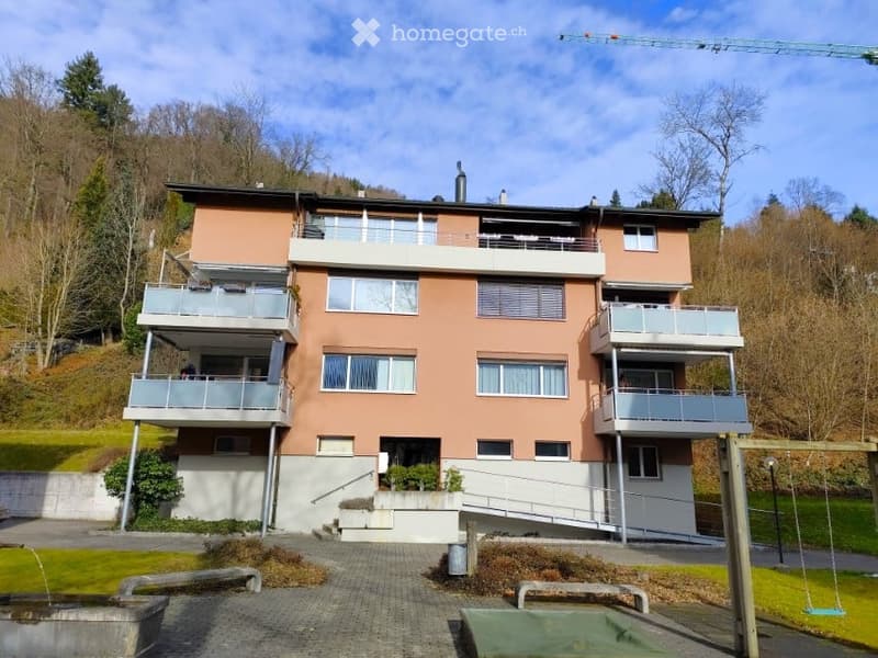 3 story apartment building, balconies, large windows, green grass, trees, swing