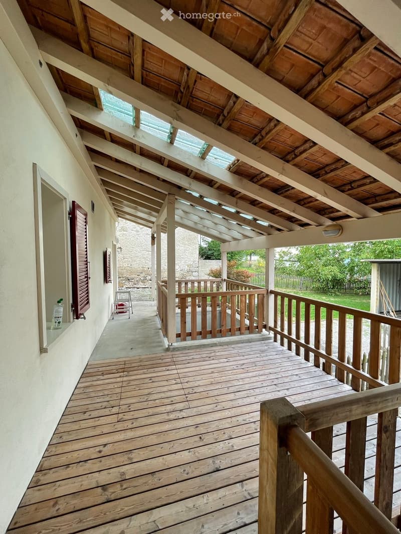 Wooden balcony with exposed wooden beams and a wooden railing, overlooking a green garden area.