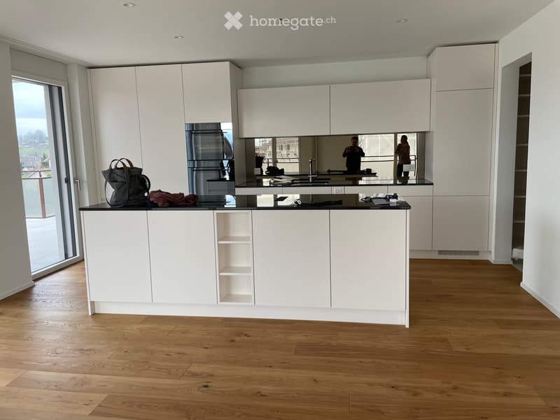 Modern kitchen with white cabinets, black countertop, and wooden flooring. A handbag and some items are placed on the counter.