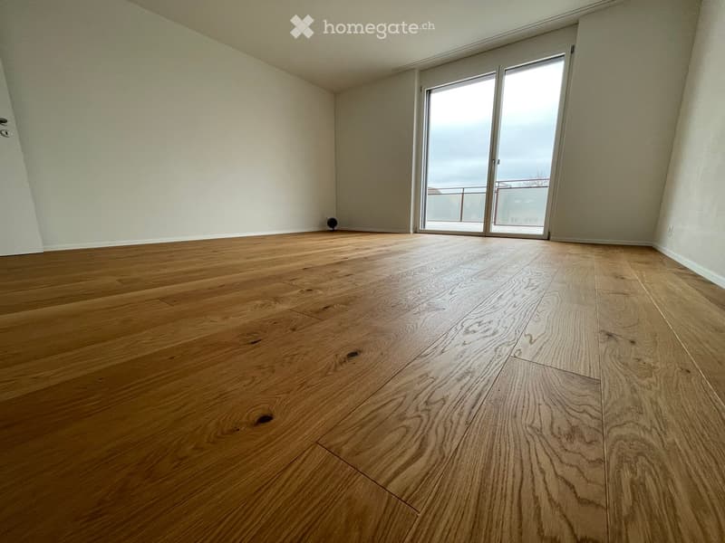 Empty room with wooden flooring and large sliding glass doors leading to a balcony.