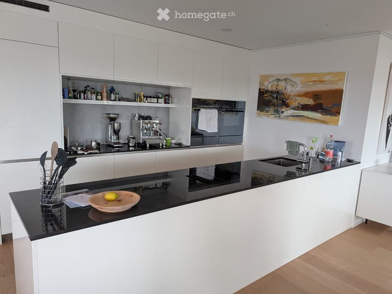 Modern kitchen with white cabinets, black countertops, and stainless steel appliances. Features a sink, coffee maker, and various kitchen utensils.