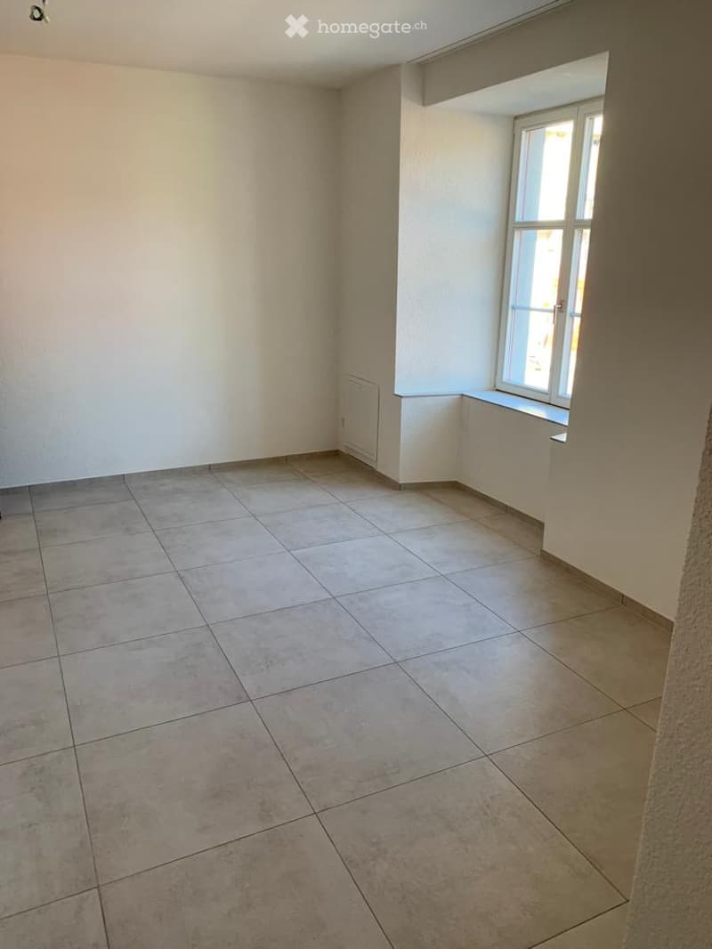 Empty room with tiled floor and white walls, featuring a single window with a white frame and a radiator below it.