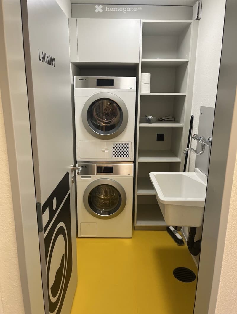 Modern laundry room with yellow flooring, white cabinets, a washing machine, dryer, sink, and shelves for storage.