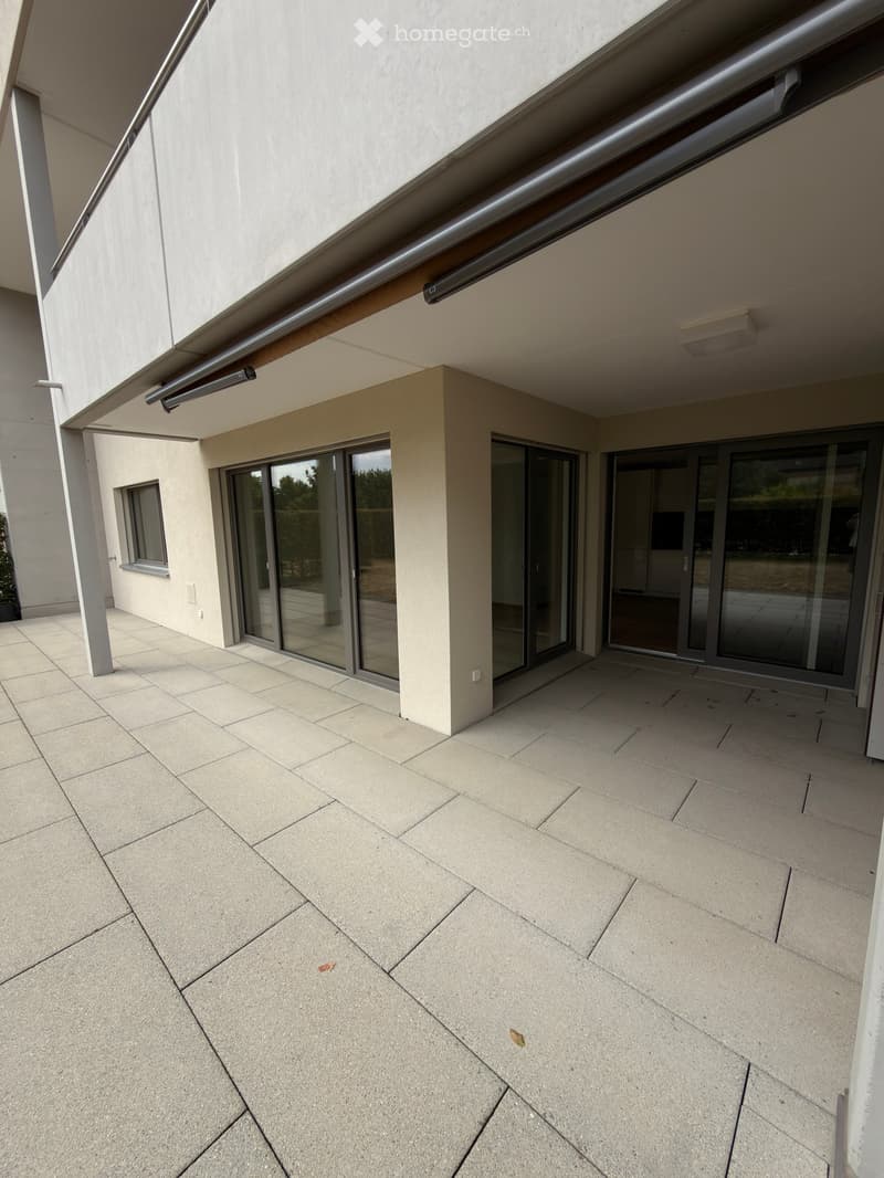Modern balcony with large sliding glass doors, tiled floor, and covered area with a metal awning.