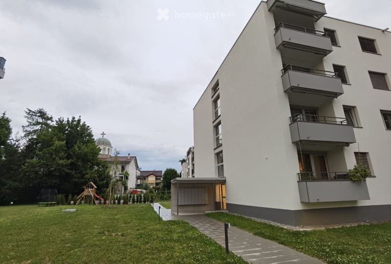 Modern multi-story residential building with balconies, surrounded by a grassy area and playground equipment.