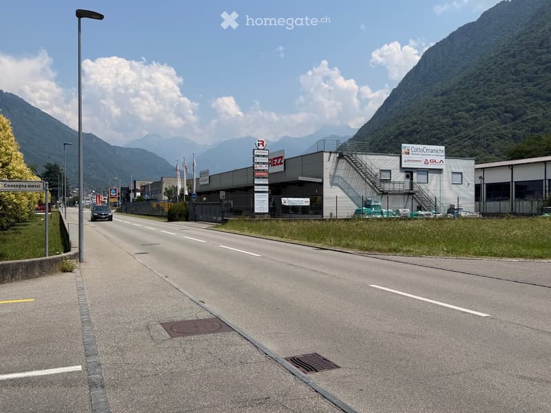 Modern industrial building with signage, surrounded by a road and mountains in the background.