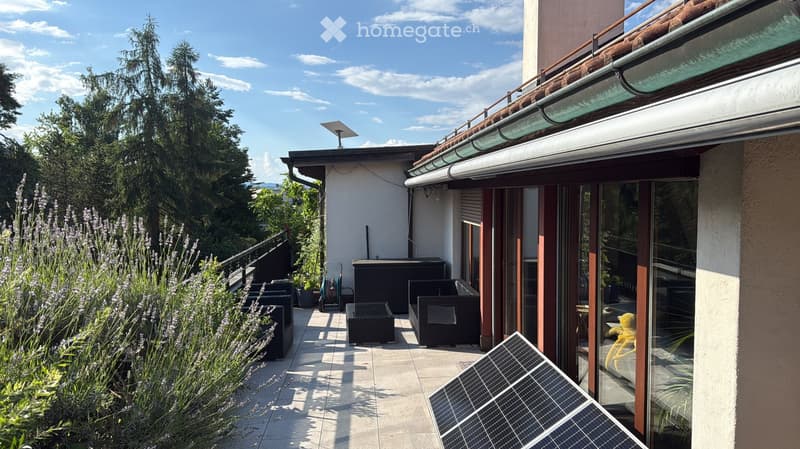 Balcony with outdoor furniture, including a sofa, table, and chairs, surrounded by greenery and a view of the landscape.