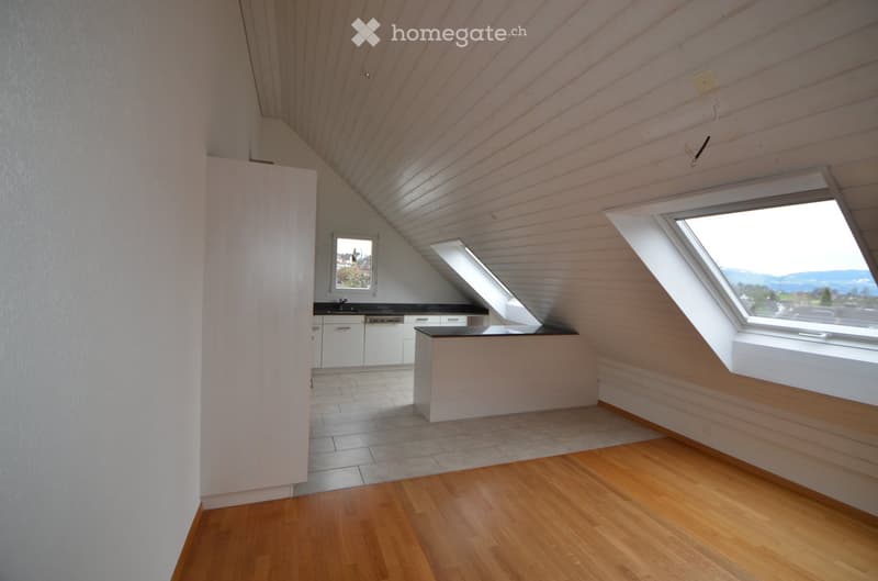 Bright, modern kitchen with wooden floors, white cabinets, and a black countertop. Features large skylight windows and a small seating area with a table.