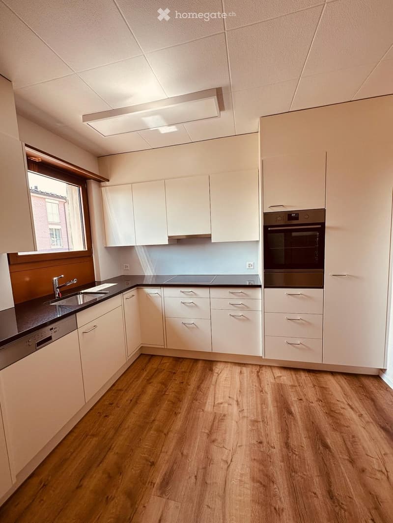 Modern kitchen with white cabinets, wooden flooring, and stainless steel appliances including a sink, oven, and dishwasher.