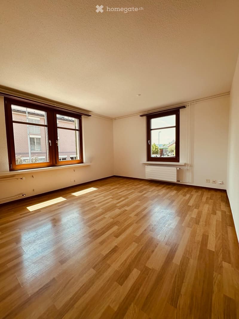 Empty room with wooden flooring, large windows, and radiators under the windows.