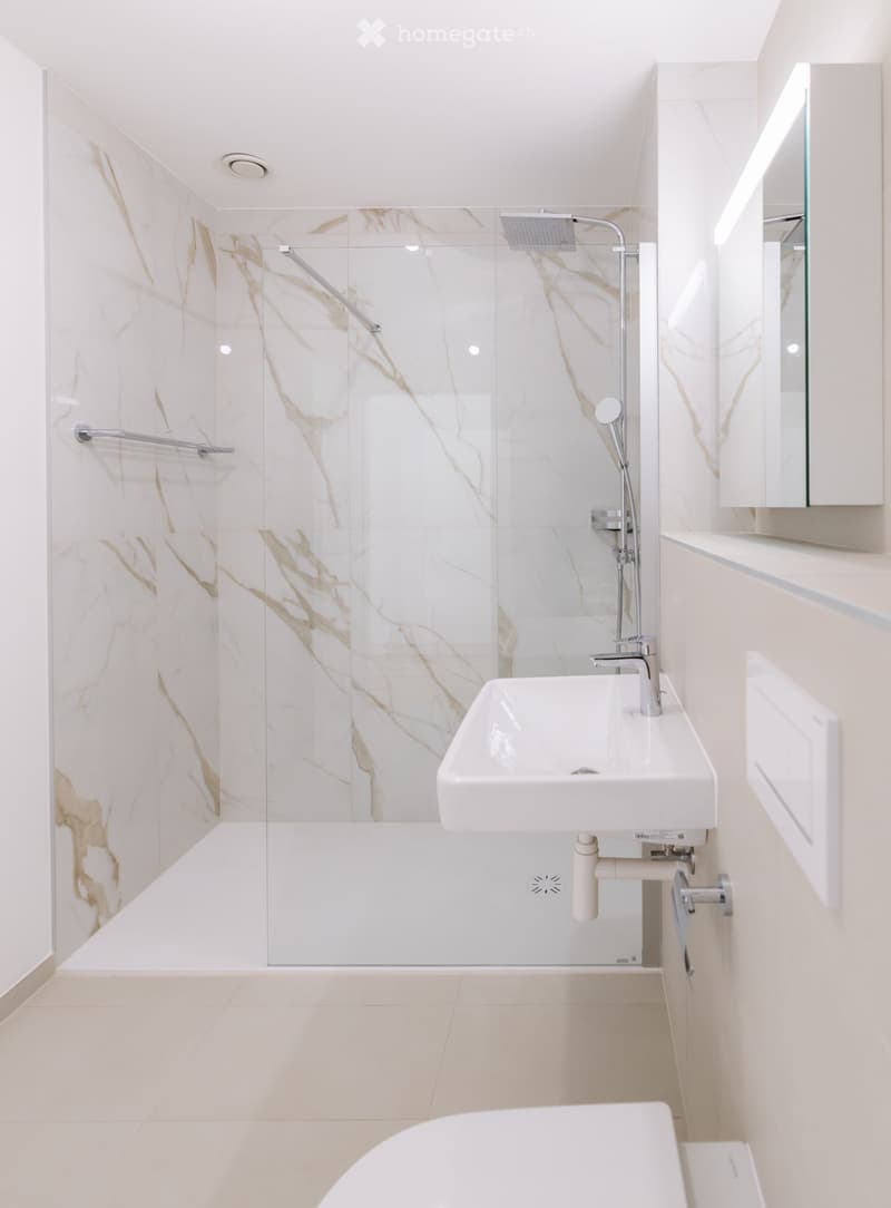 Modern bathroom with white marble tiles, a glass-enclosed shower, a white sink, and a bathtub.
