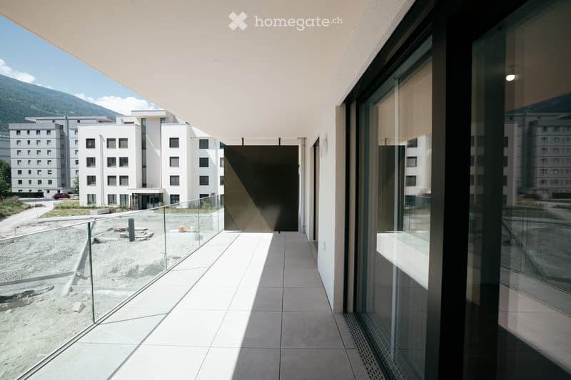 Modern balcony with glass railings, tiled floor, and a view of a construction site and modern buildings in the background.