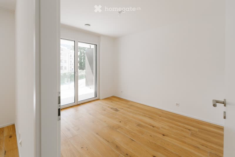 Empty room with light wooden flooring, white walls, and large glass sliding doors leading to a balcony.