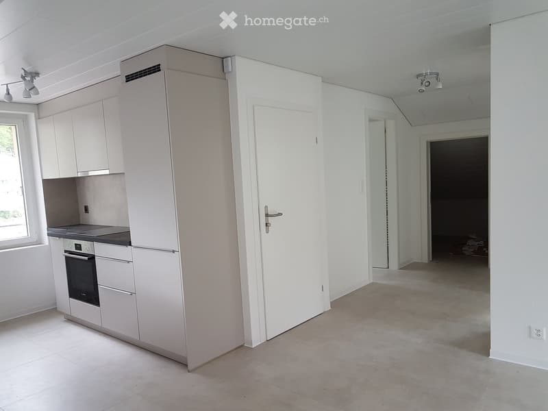 Empty kitchen area with white cabinets, a built-in oven, and a refrigerator. The space is clean and unfurnished, with tiled flooring and white walls.