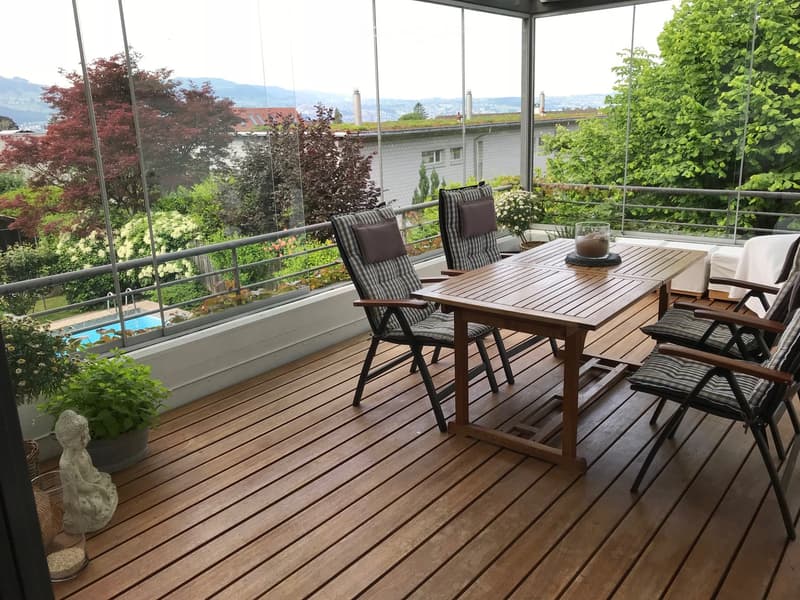 Wooden deck with a table, chairs, and potted plants, offering a scenic mountain view.