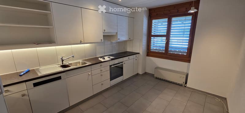 Modern kitchen with white cabinets, stainless steel sink, oven, and countertop. Features a window with blinds and built-in lighting under the cabinets.