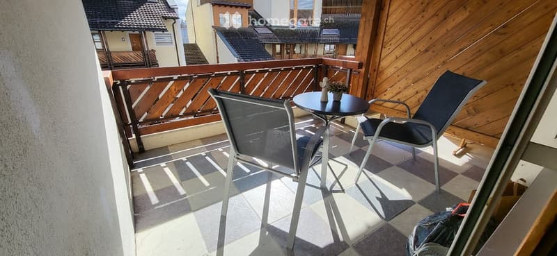 Balcony with wooden railing, tiled floor, two chairs, small round table, and small plant.