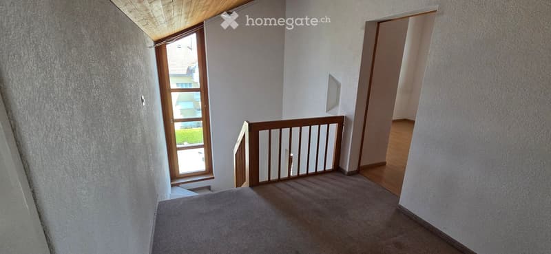 Staircase with wooden railing, carpeted steps, and a window overlooking a garden area.
