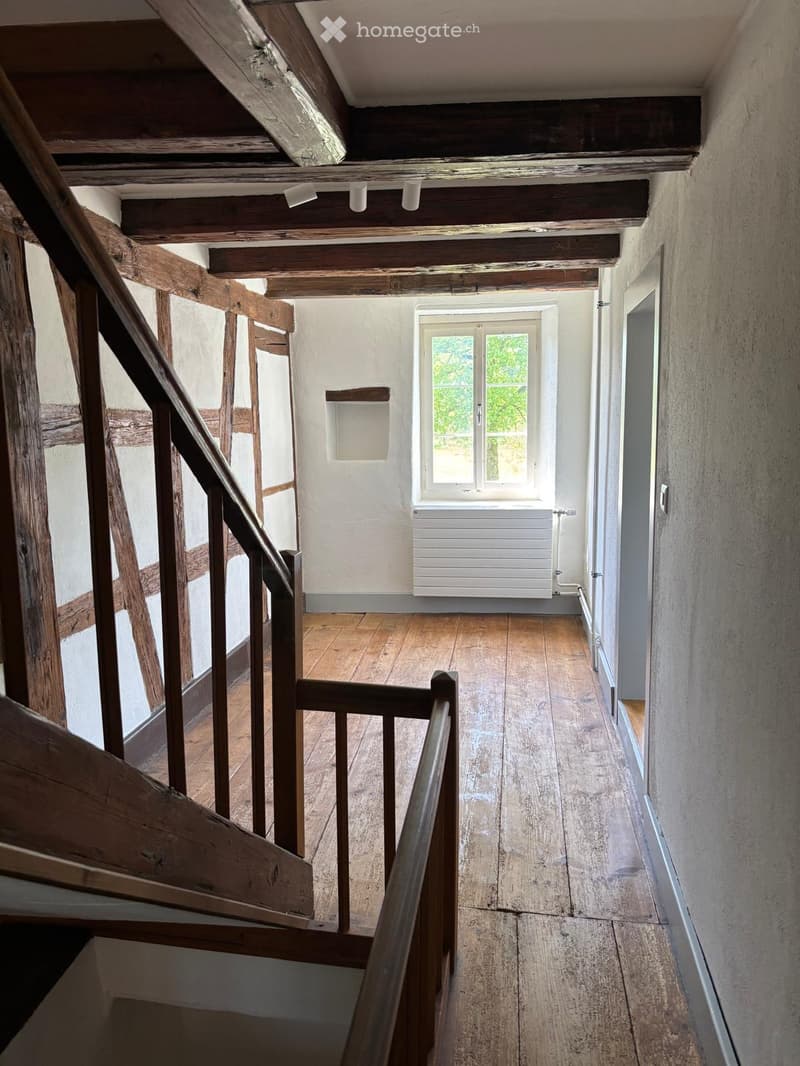 Empty wooden hallway with exposed beams, wooden floor, and a window at the end.