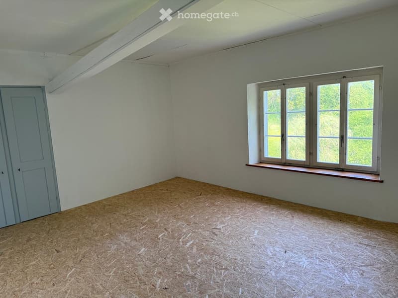 Empty room with light grey walls, wooden floor, single door, and large window with wooden sill.