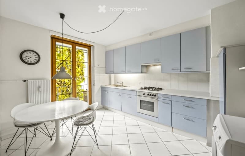 Modern kitchen with light blue cabinets, white countertops, and stainless steel appliances. Includes a dining area with a white table and chairs.